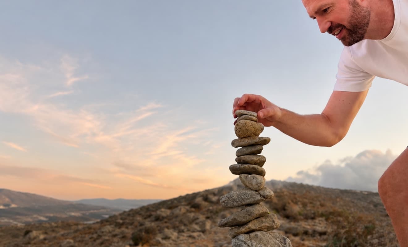 Roy van Sichem, oprichter van Awaren en mindfulnesstrainer, stapelt stenen bij zonsondergang